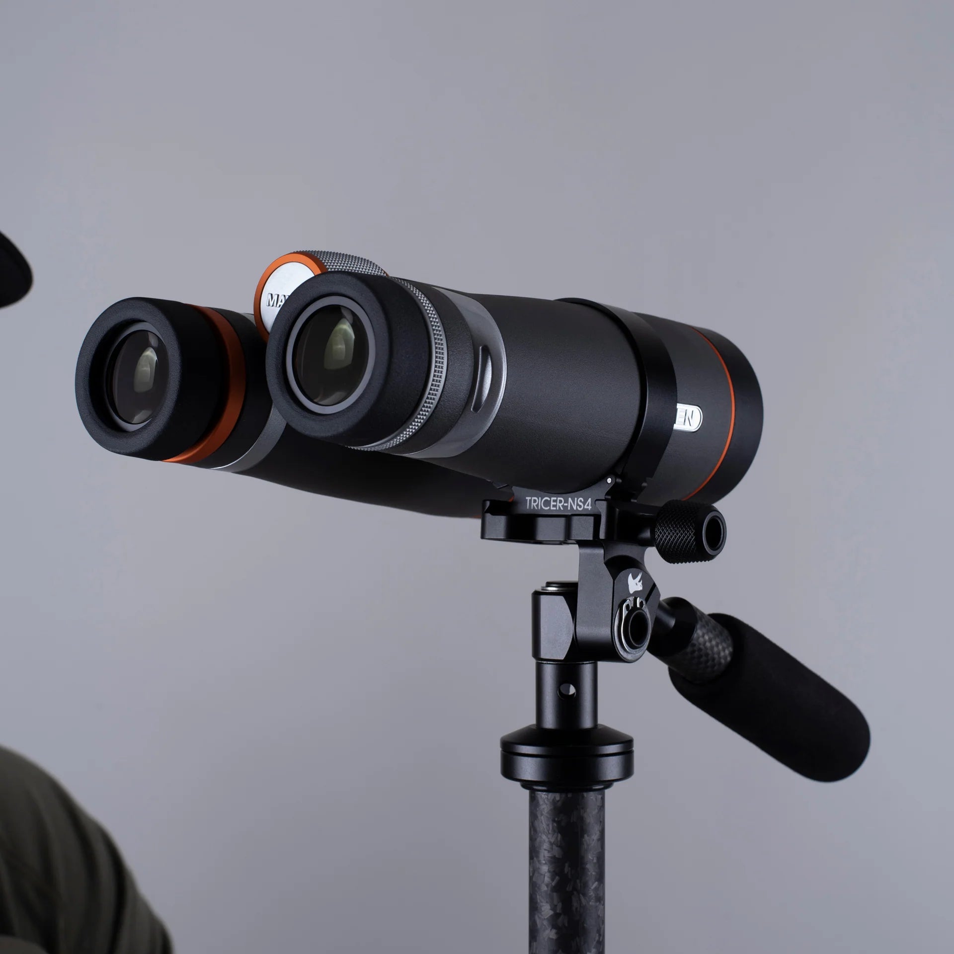 Binoculars mounted on a tripod using an Arca-Swiss adapter against a gray background