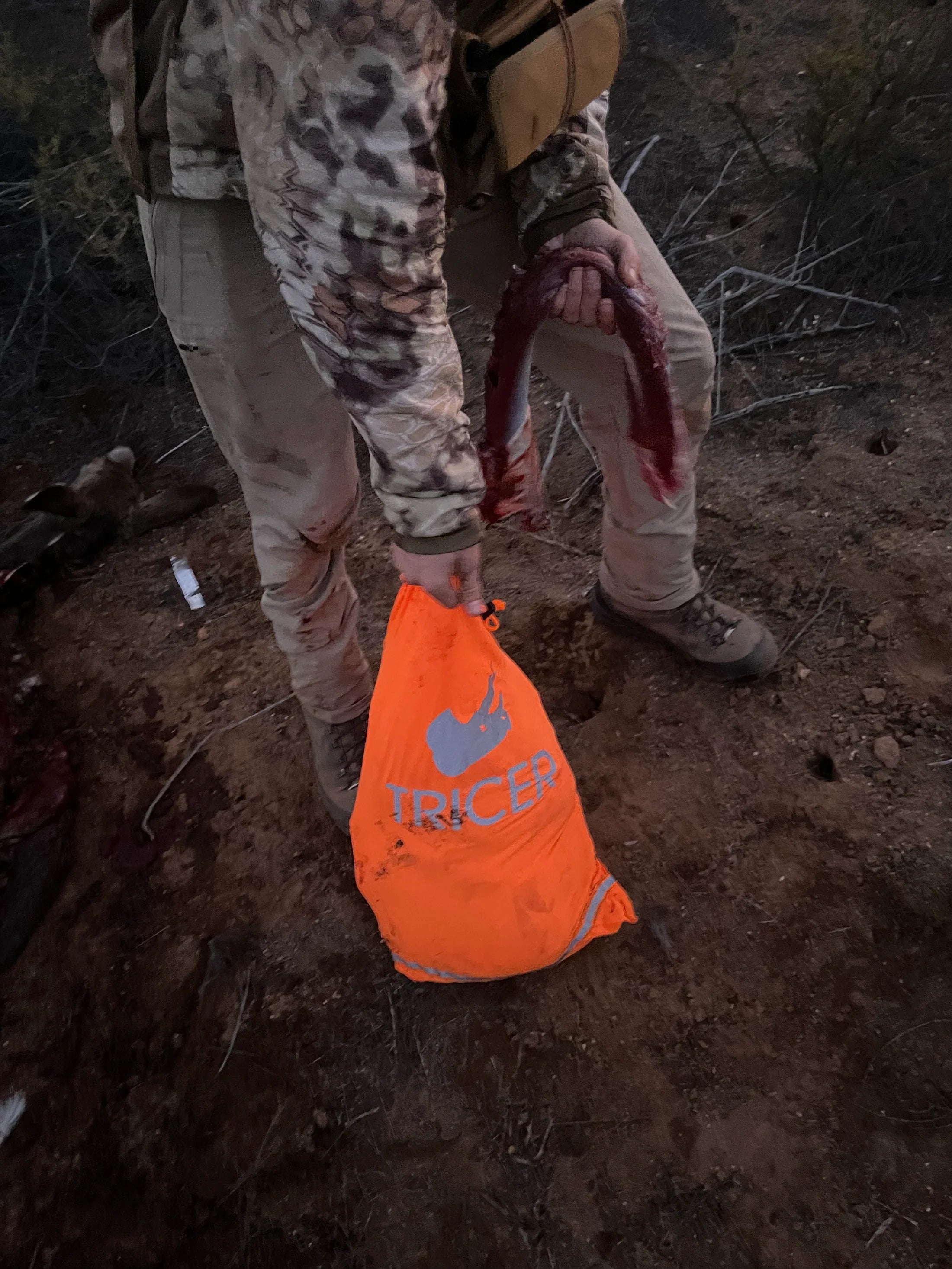 Man holding an orange bag with a TRICER logo in a natural setting