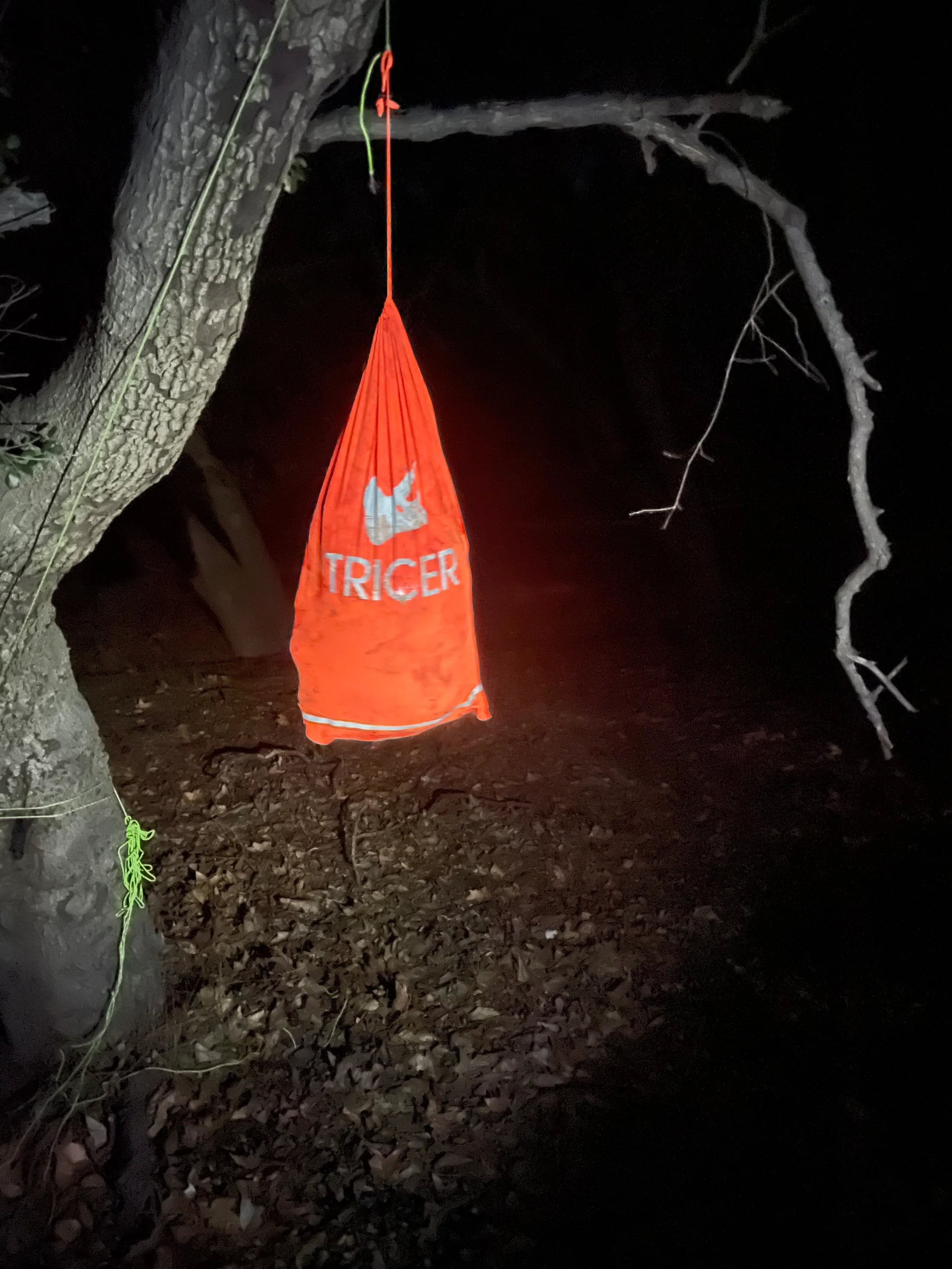 Orange bag with 'TRICER' branding hanging from a tree at night.