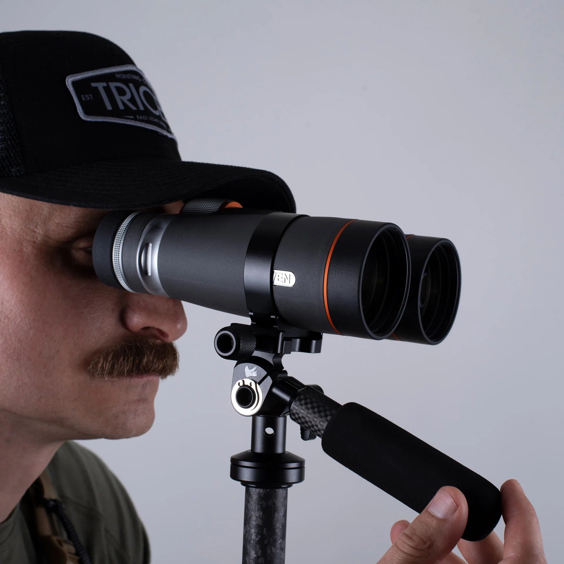 Man using binoculars on a tripod against a plain background